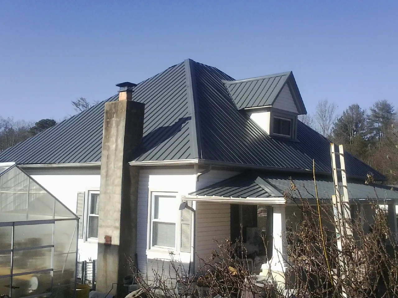 Dark blue standing seam metal roof on a white farmhouse with dormer — Slate & Tile Roof Repair by Roofing Brothers in Bonanza