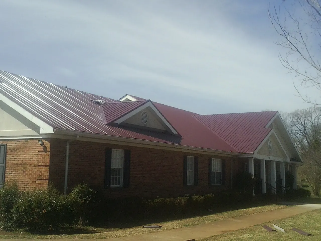 Red metal roof with gabled entries on a long brick building, from a Hail Damage Roof Repair job in Bonanza