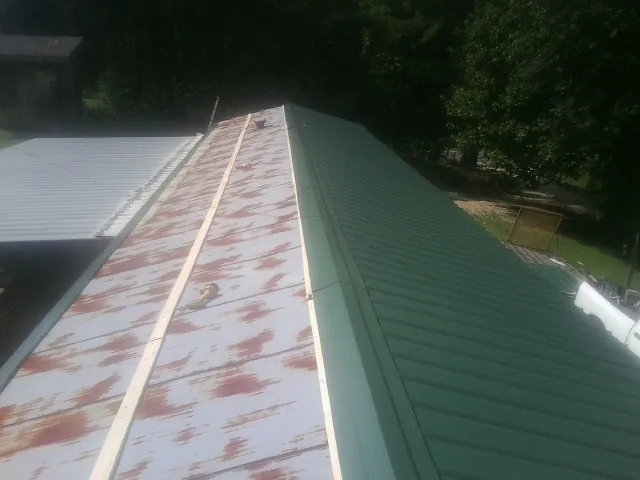 Old rusted panels beside newly installed green metal roofing — Wind Damage Roof Repair by Roofing Brothers in Bonanza