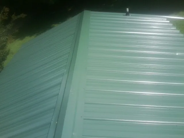 New green metal panels meeting at the ridge of a roof — Flat Roof Repair work by our crew in Bonanza