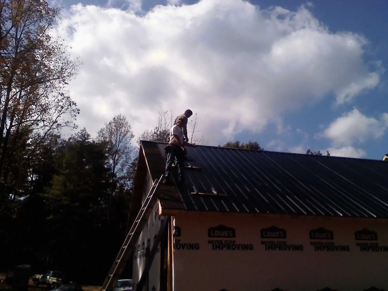 Roofer fastening dark metal panels high against a cloudy sky, from a Roof Inspection job in Bonanza