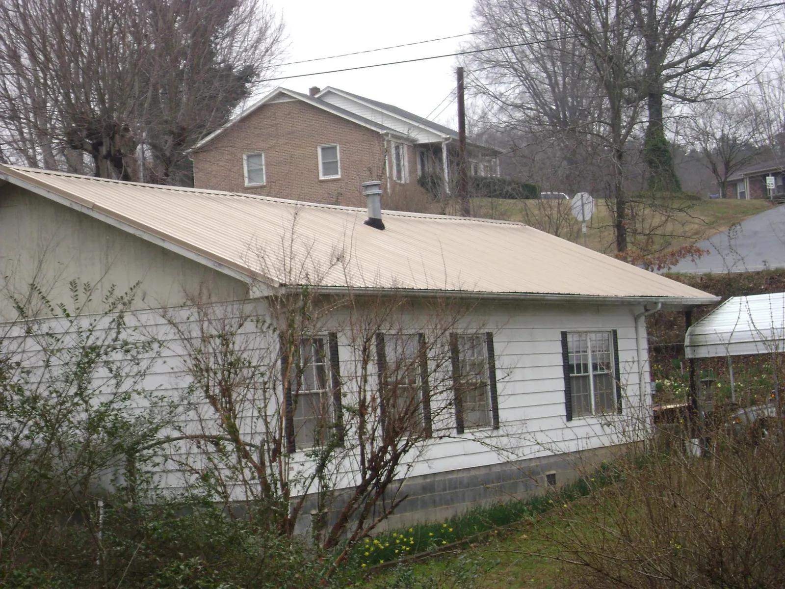 Tan metal roof on a white sided house set into a hillside — Commercial Roofing by Roofing Brothers in Bonanza