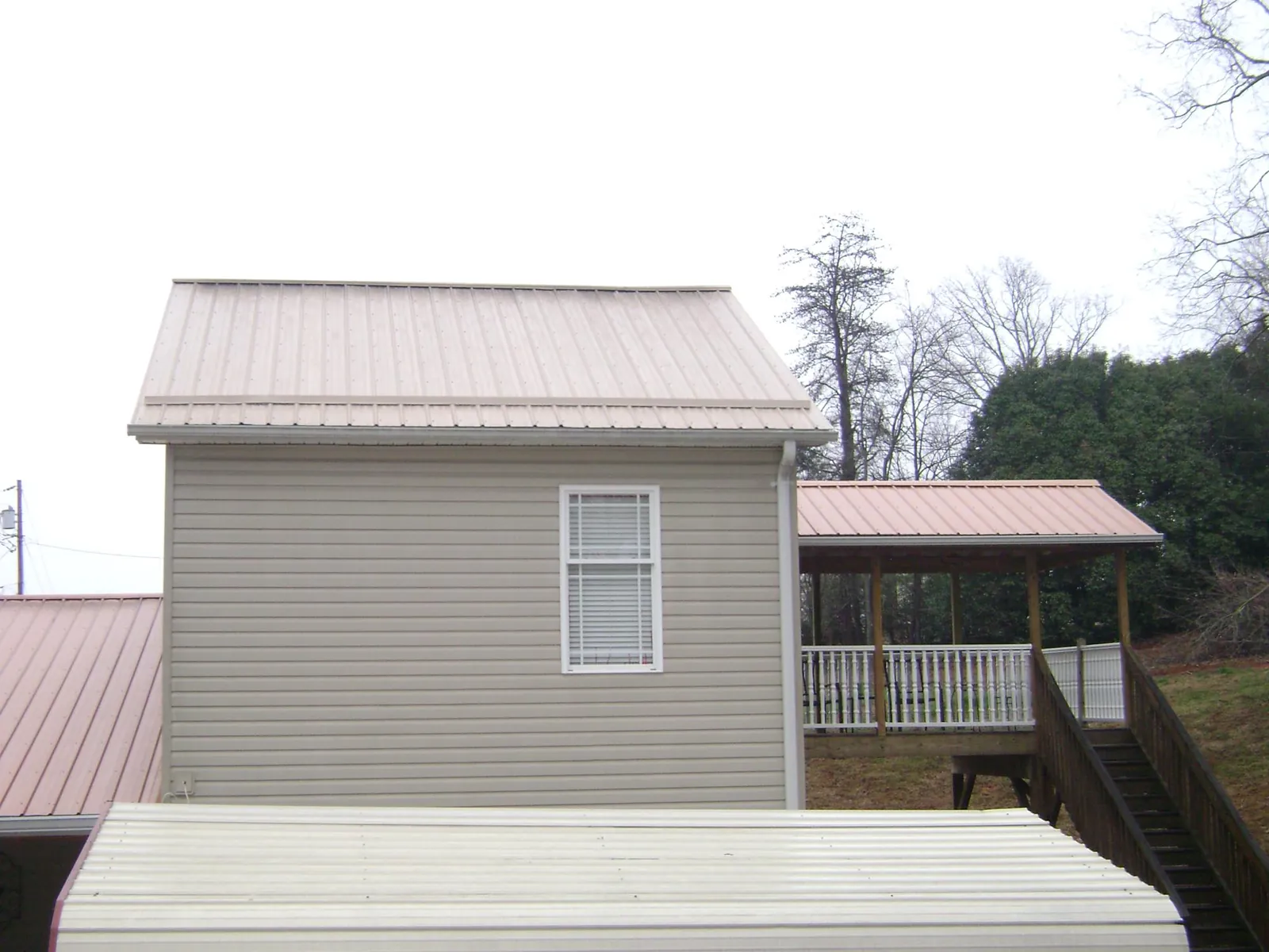 Tan metal roofs on a two story addition and attached porch, from a Roof Replacement job in Bonanza